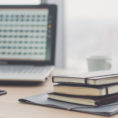 A photo of documents on an office table next to a pen and a laptop.