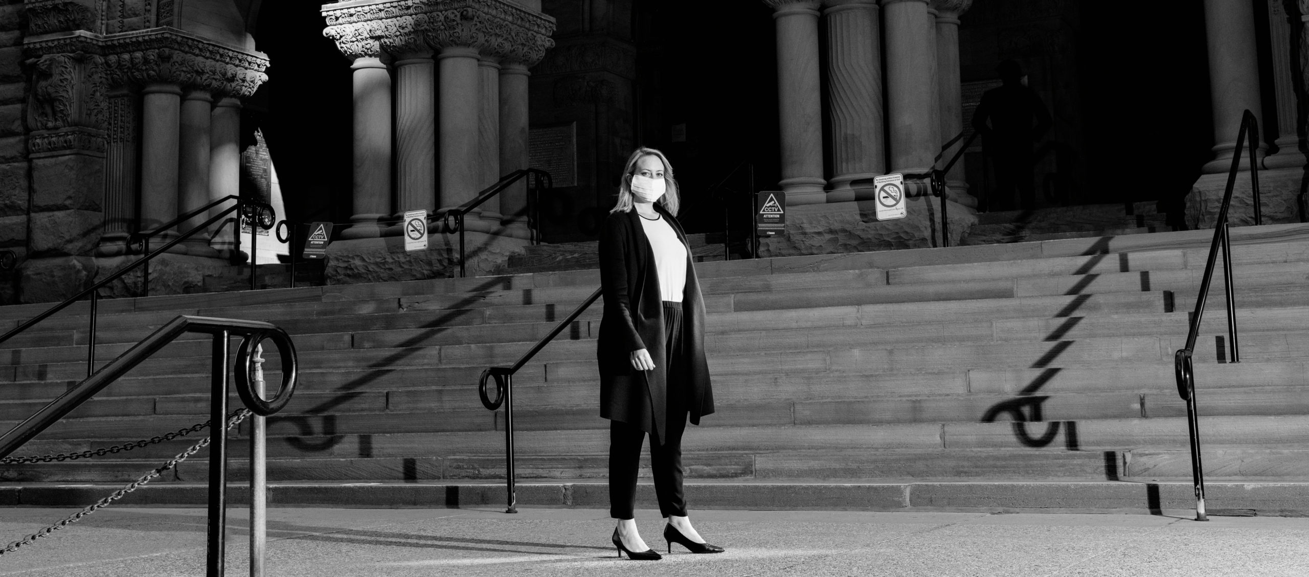Black and white photo of Lisa Jørgensen wearing a mask and standing in front of Old City Hall