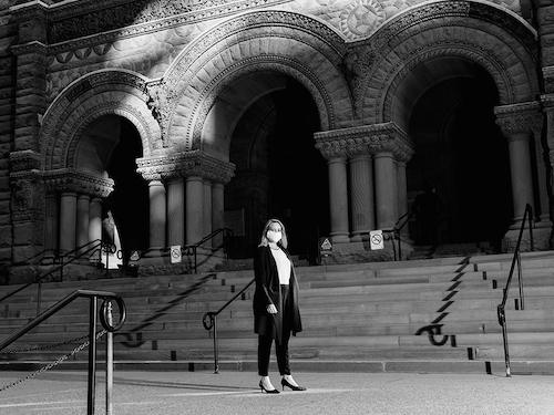 Black and white photo of Lisa Jørgensen wearing a mask and standing in front of Old City Hall