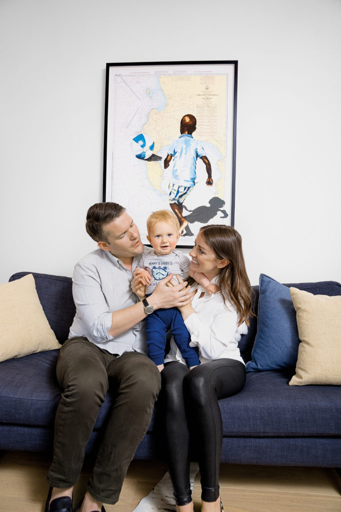 Portrait of Larissa and Brad Vermeersch sitting on the couch in their home with baby Teddy