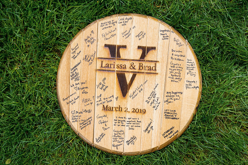 An image of a whiskey barrel lid with Larissa & Brad's initials and signatures from wedding guests