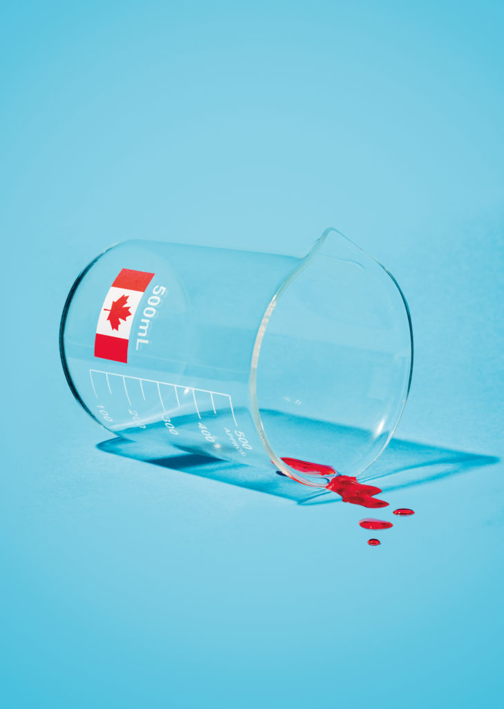 An image of a 500ml beaker with a Canadian flag on it that's tipped over with a few drops of red liquid spilling out