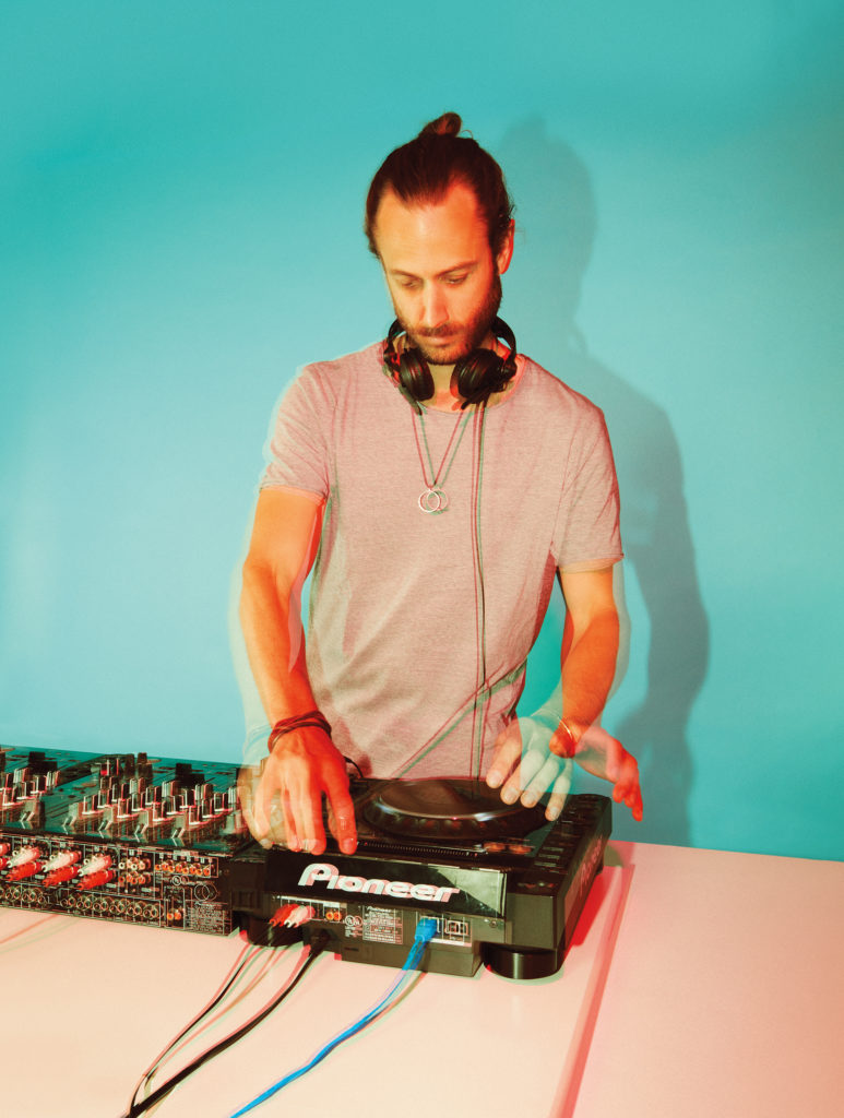 Varoujan Arman standing with headphones around his neck, using the turntable on his DJ table