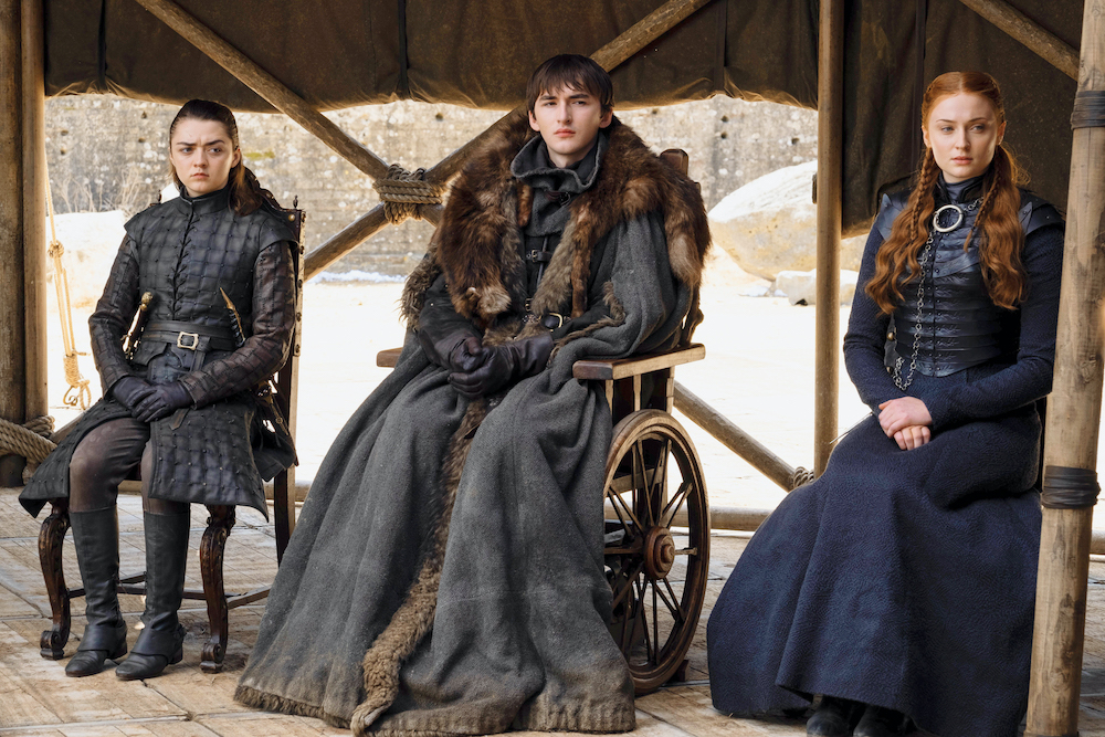 Scene from Game of Thrones, three characters sit on a wooden stage