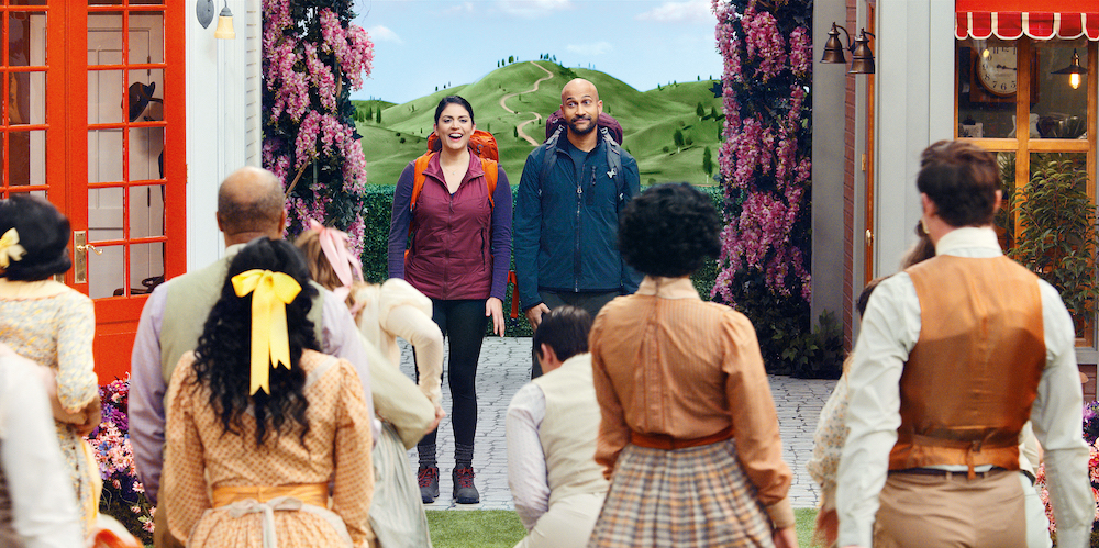 Scene from the film Schmigadoon! featuring Starring Keegan- Michael Key and Cecily Strong, standing with backpacks on talking to a group of people