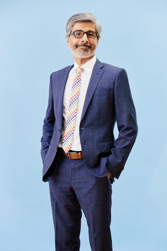 Portrait of Kumail Karimjee standing against a blue background