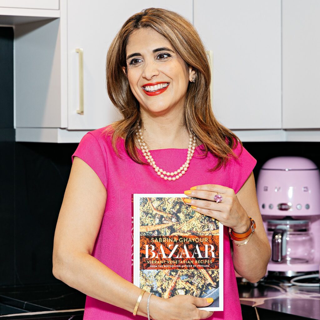 Leila Rafi standing in her kitchen holding a Persian cookbook
