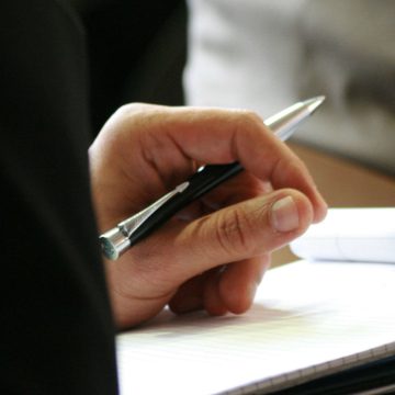 An image of a hand holding a pen and paper.