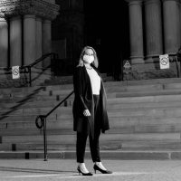 Black and white photo of Lisa Jørgensen wearing a mask and standing in front of Old City Hall