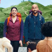 Scene from the film Schmigadoon! featuring Starring Keegan- Michael Key and Cecily Strong, standing with backpacks on talking to a group of people